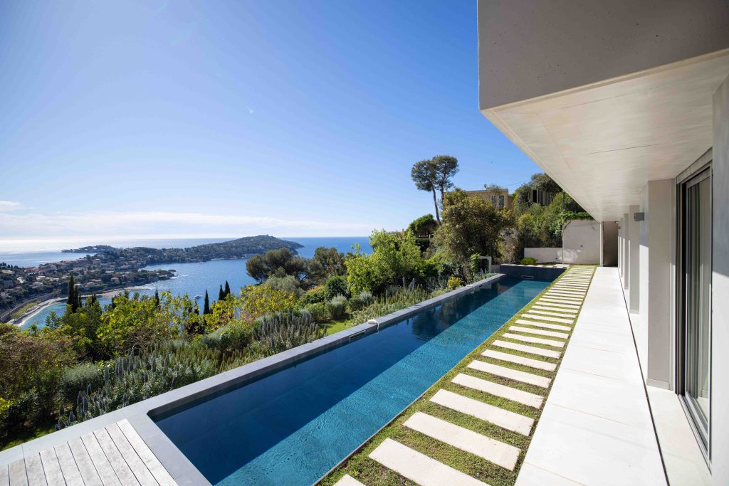 Longue piscine design face à la mer avec jardin méditerranéen et vue sur la presqu’île de Saint-Jean-Cap-Ferrat depuis une villa luxueuse de Vista Magnifika